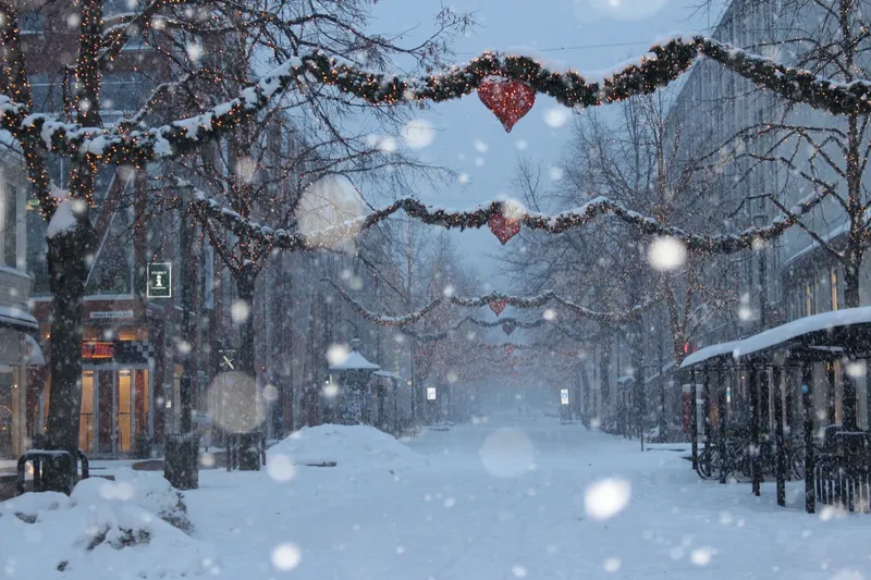 Snowfall in a Christmas-decorated street in central Trondheim — garlands and red hearts strung above the street